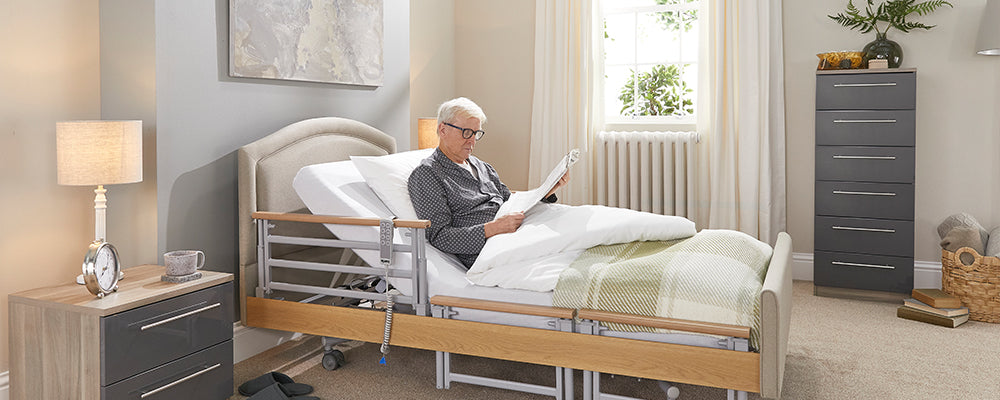 Older gentlman sat reading the newspaper in bed with his glasses on 