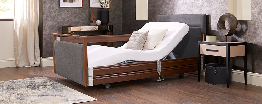 A grey and brown profiling care bed with the back rest raised in a bedroom