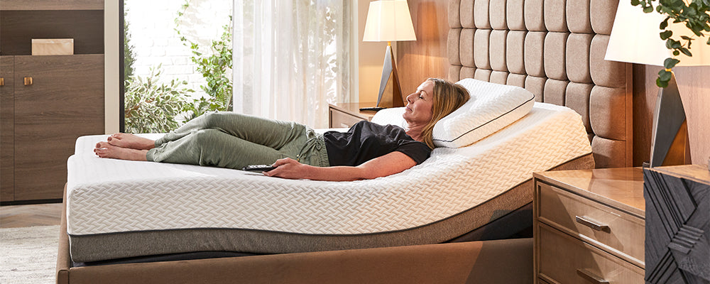 older woman with long brown hair laying on an Opera adjustable bed in zero-gravity position holding the remote control in her hand