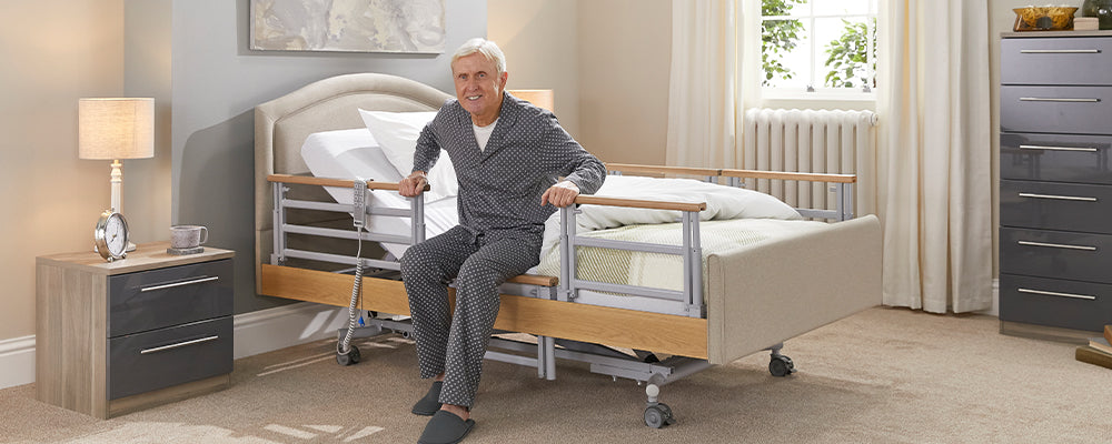 Older gentleman in grey pajamas sat on a profiling bed with his hand on the side rail