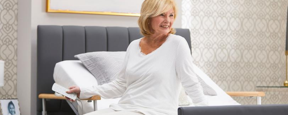 Woman seated on the Opera® Solo Comfort Plus Profiling Bed with split side rails