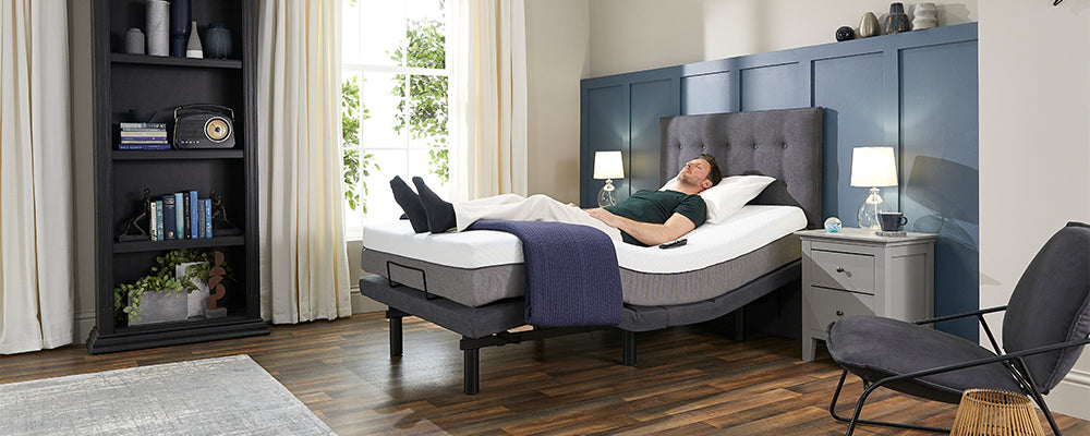 A man with brown hair laid asleep with his legs raised on an adjustable bed with a grey headboard