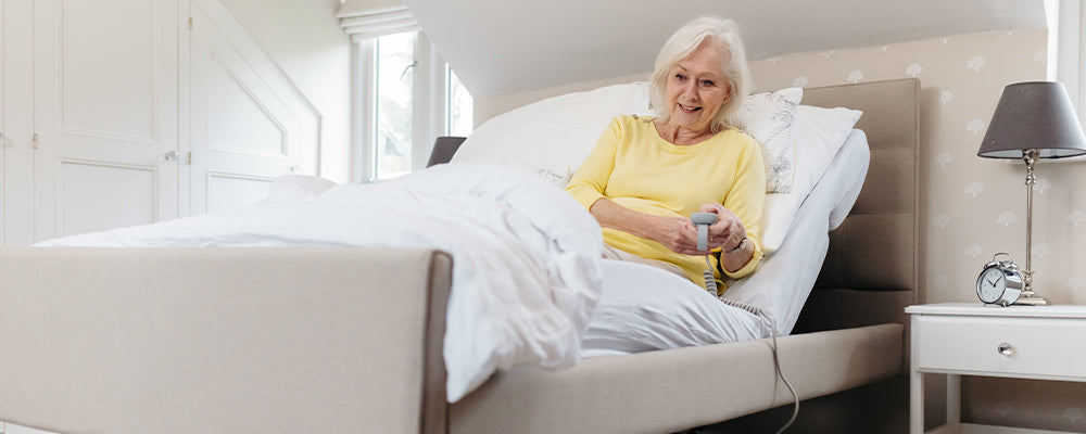 Elderly woman sat upright in bed with the back rest raised and looking down at the bed