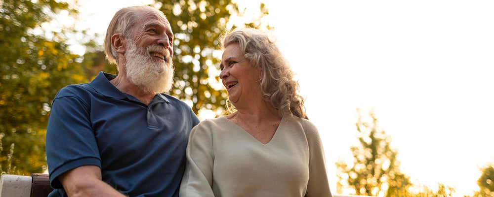 A older couple sat on a park bench smiling