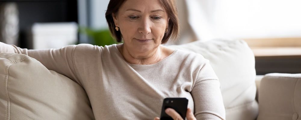 woman with brown hair sat on the sofa looking at her mobile phone