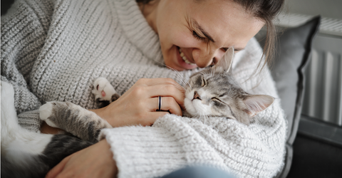 Woman cuddling her grey cat in her arms, smiling.