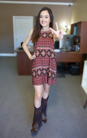 Brunette woman wearing a red print dress and fringe cowgirl boots