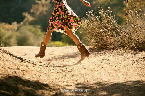 a girl in a floral dress wearing cowboy boots running on the dirt