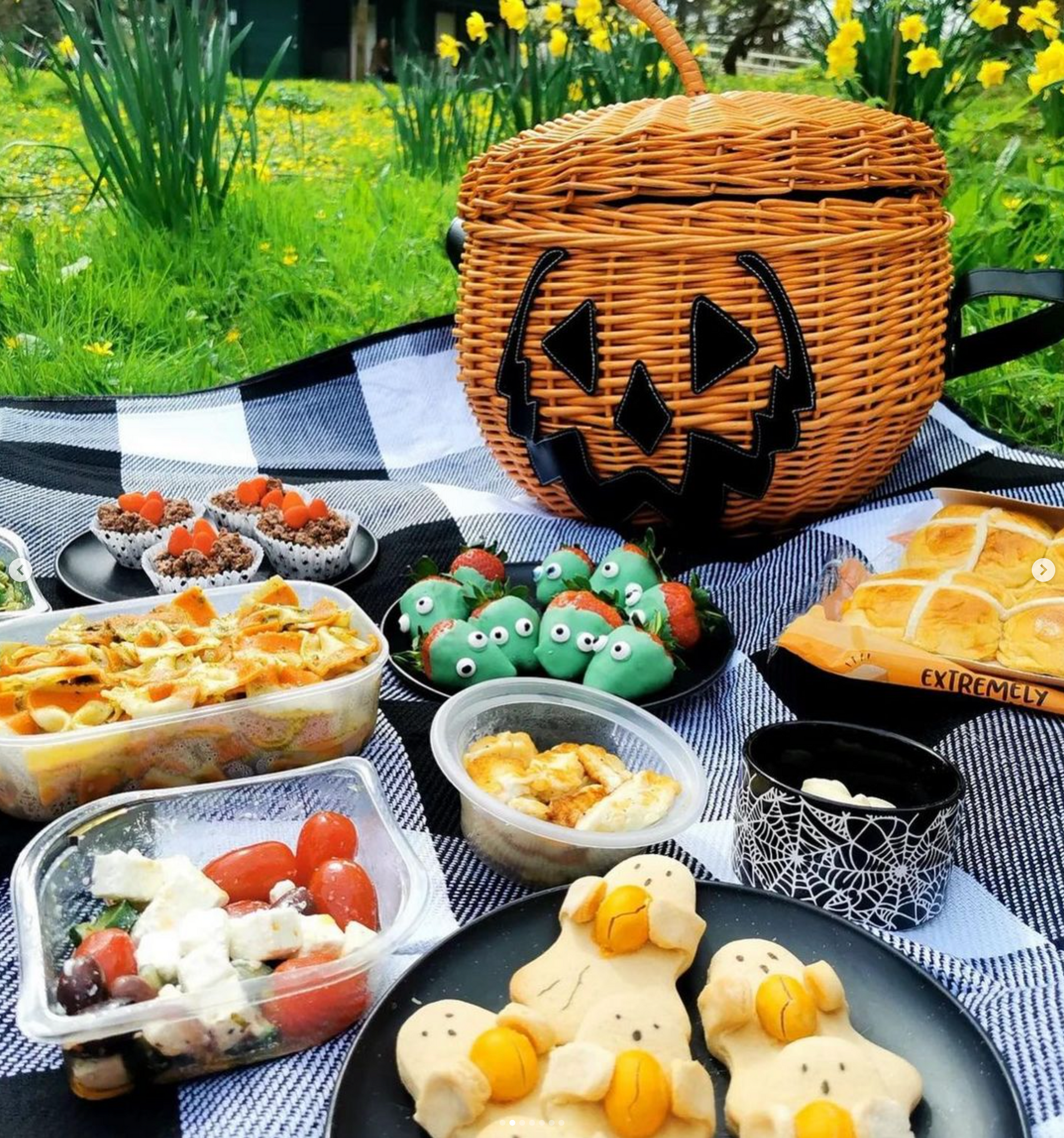 Easter-ween easter ween easter halloween themed picnic with spooky strawberries, salads and a jack-o-lantern pumpkin shaped wicker basket on grass.