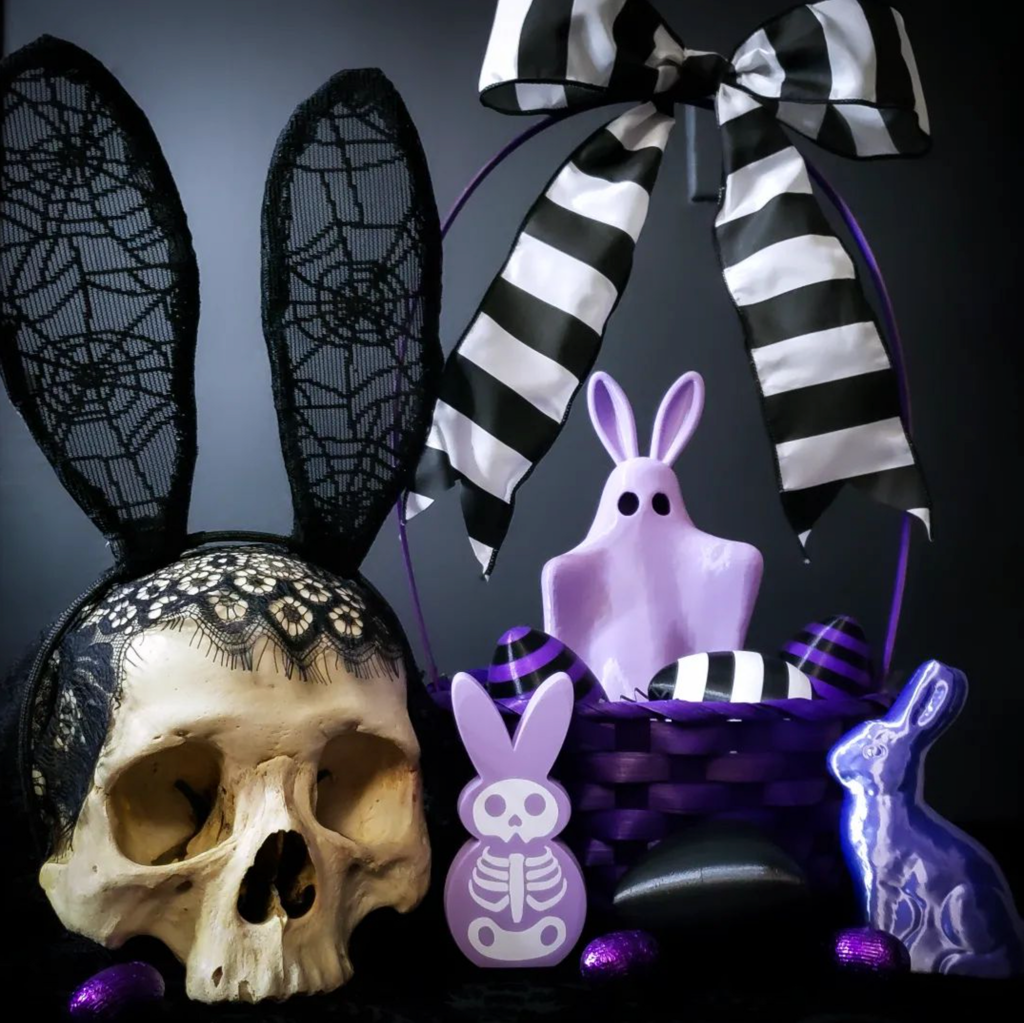 A spooky easter, easterween, easter-ween, easter ween, halloween easter table decorations of a skull wearing black lace bunny ears a purple spooky peep figure, shiny purple bunny decoration, black and purple easter basket with beetlejuice striped eggs and a black and white stripe bow.