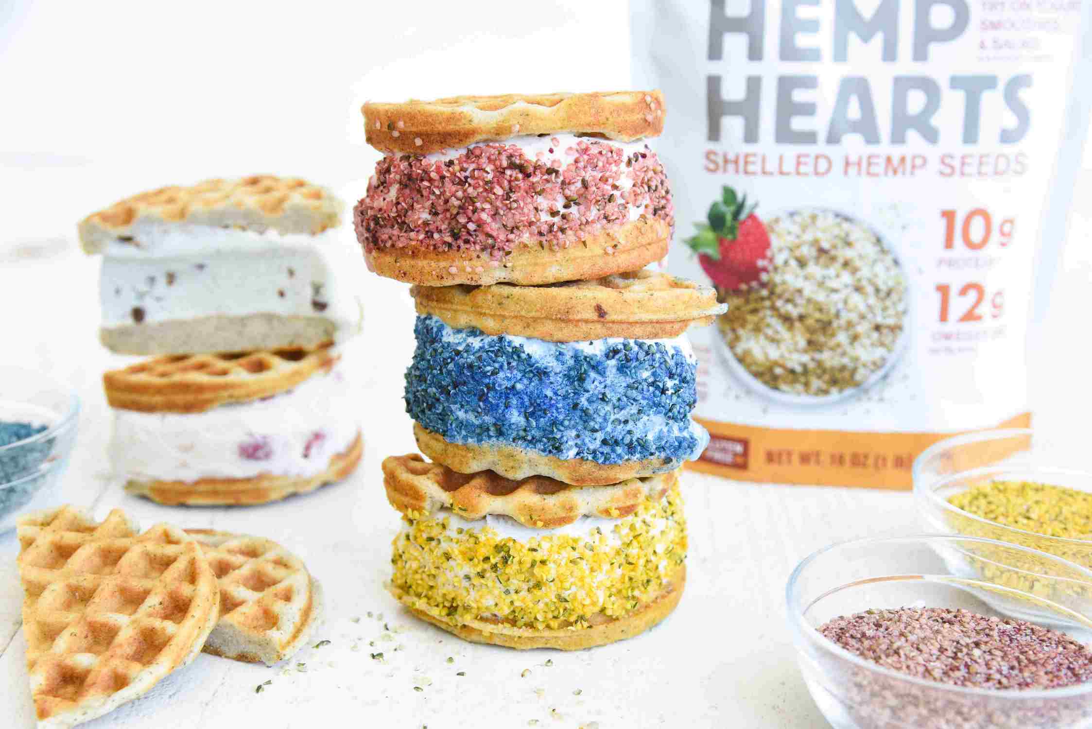 stack of three ice cream waffle sandwiches decorated in pink, blue and yellow hemp hearts in front of a bag of Manitoba Harvest Hemp Hearts.