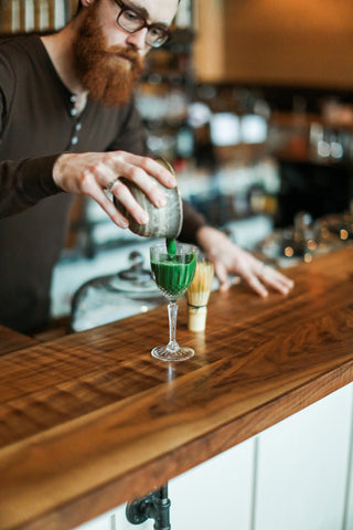 Man pours matcha green tea into cocktail glass at a fancy bar