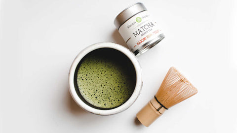 cup of matcha tea with whisk and mizuba brand matcha container