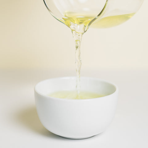 Japanese tea is poured from a glass pot into a white teacup