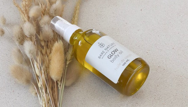 Glass Bottle of golden body oil laying on stone counter with dry grasses