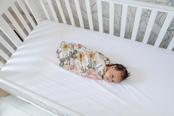 baby girl swaddled in a vintage floral swaddle in a crib
