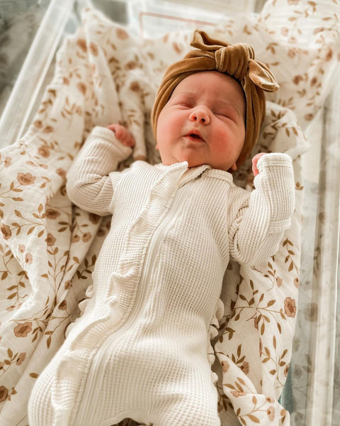 a newborn baby girl in a waffle ruffled onesie bodysuit on a soft muslin receiving blanket with pretty wild flowers.