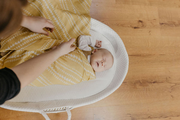 newborn baby boy being swaddled in a yellow geo muslin blanket