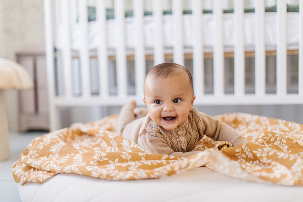 baby boy is having tummy time on a yellow orange leafy sprig baby blanket in a clean baby room