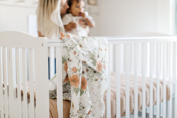 mama hugging a baby in the babies nursery room, the room is light and tidy with a pretty floral swaddle hanging from the crib