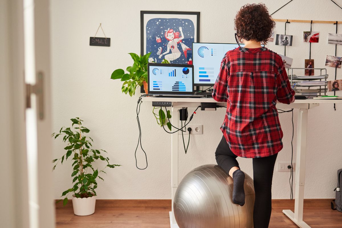 Woman using standing desk while resting on a yoga ball.