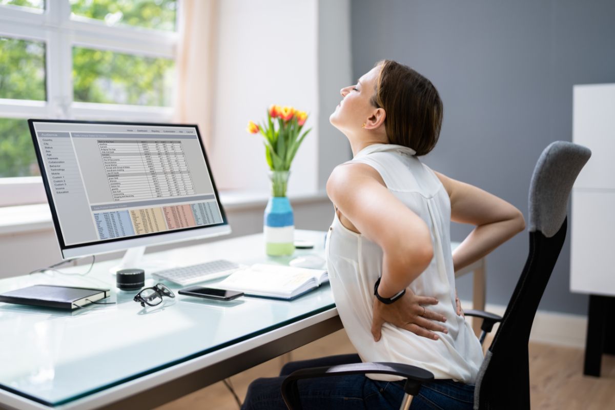 Woman with painful back while sitting at a desk.