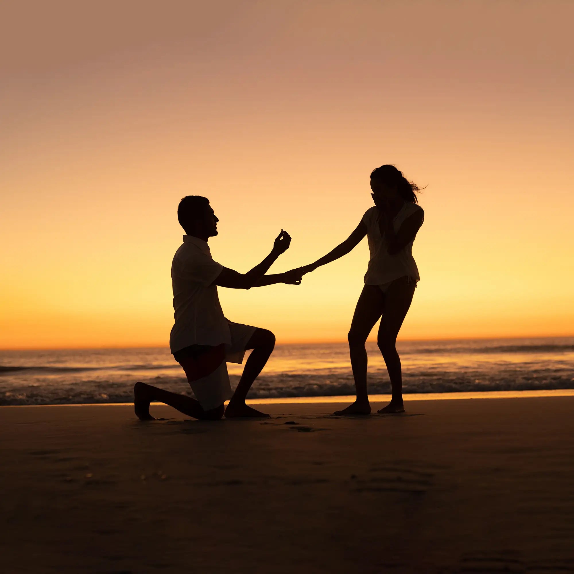 Man proposing ring to woman on the beach at sunset evening