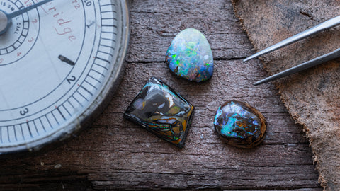 Three boulder opals are displayed on a textured wooden background