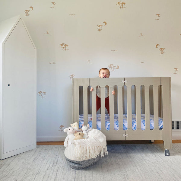 baby standing in beach house grey crib