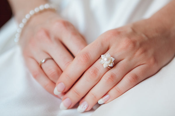 Manos cruzadas con fondo de vestido blanco para resaltar anillo con perlas que tiene en mano izquierda del dedo del medio