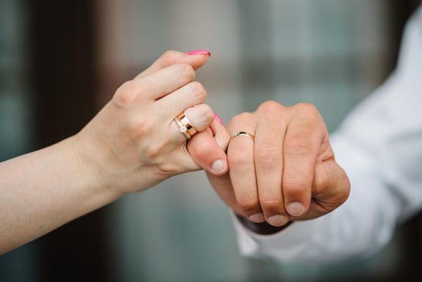 Pareja agarrados de un dedo mostrando sus anillos de compromiso en color oro