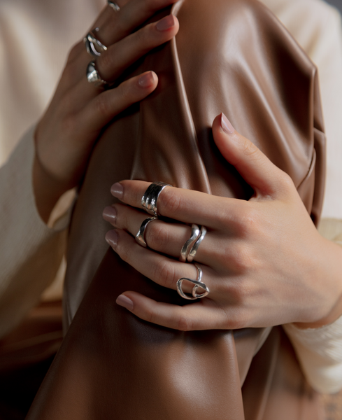 Mujer agarrando su rodilla con sus manos para resaltar que tiene varios anillos en diferentes dedos de las dos manos