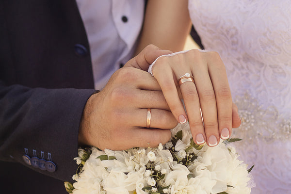 Pareja en su boda tomando sus manos y mostrando sus anillos de compromiso junto a un arreglo floral de boda