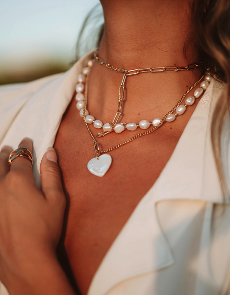 Mujer en la playa con blusa desabotonada y collares alrededor de su cuello de diferentes formas, materiales y colores que destacan y resaltan su cuello