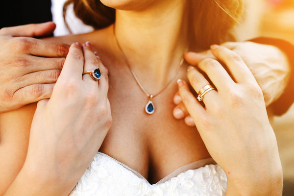 joven pareja tomados de la mano por la espalda y mostrando collar y anillos de piedras preciosas color azul