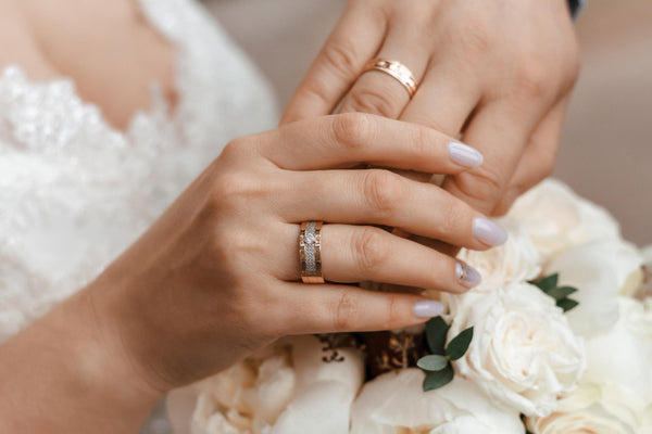 Pareja de esposos tomando sus manos apoyados sobre un ramo de flores mostrando sus anillos de compromiso