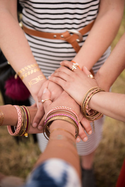 Manos entrecruzadas de cuatro mujeres que tienen varias pulseras de diferentes colores y diseños en sus manos