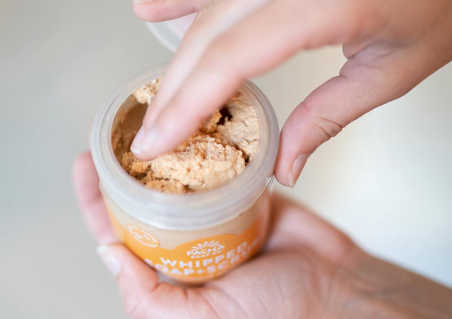 hand dipping into jar of pacha whipped soap scrub sustainable body wash