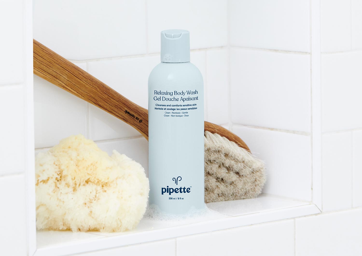 blue bottle of pipette sustainable body wash on shower shelf with bamboo brush and sponge loofah