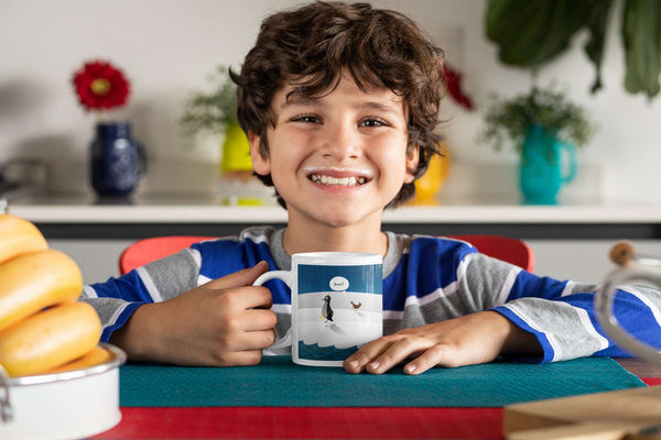 Young boy smiling with white ceramic mug with penguin kids book design by Brad Pohl