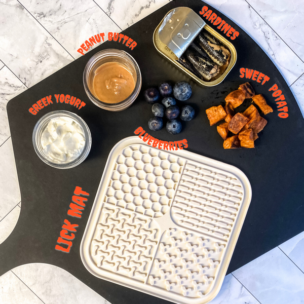 Sardine lick mat ingredients laid out on a cutting board with spooky text over top of each ingredient. Ingredients include: Greek Yogurt, Peanut Butter, Sardines, Blueberries, & Sweet Potato.