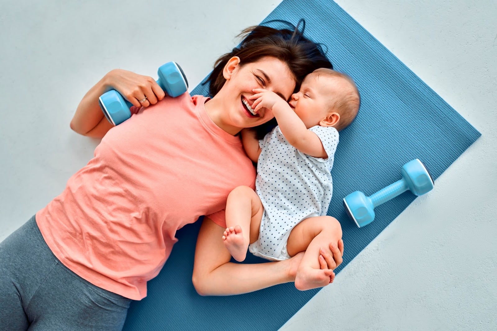 A woman lies on a mat with her baby, both relaxed and enjoying their time together.