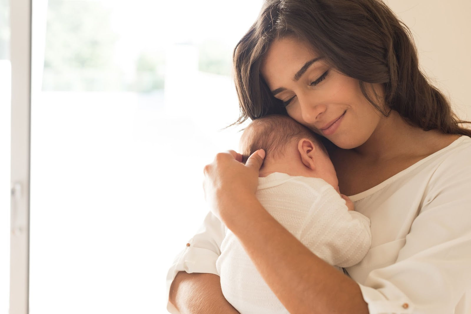 A woman tenderly holding a newborn baby close to her chest.