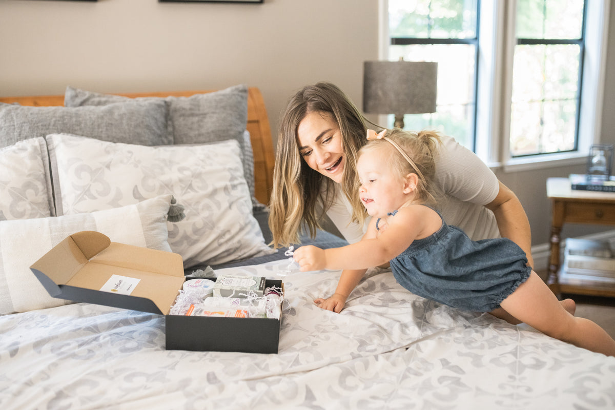 mother and baby on the bed unboxing gift package