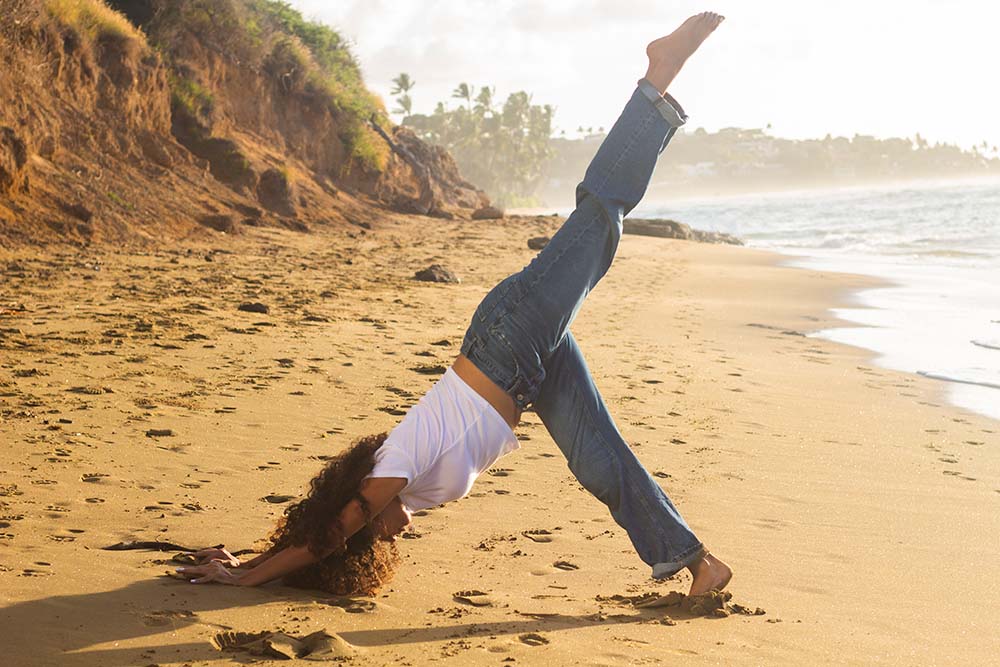 Yoga Instructor Rae doing a three-Legged downward Facing Dog yoga Pose on the beach