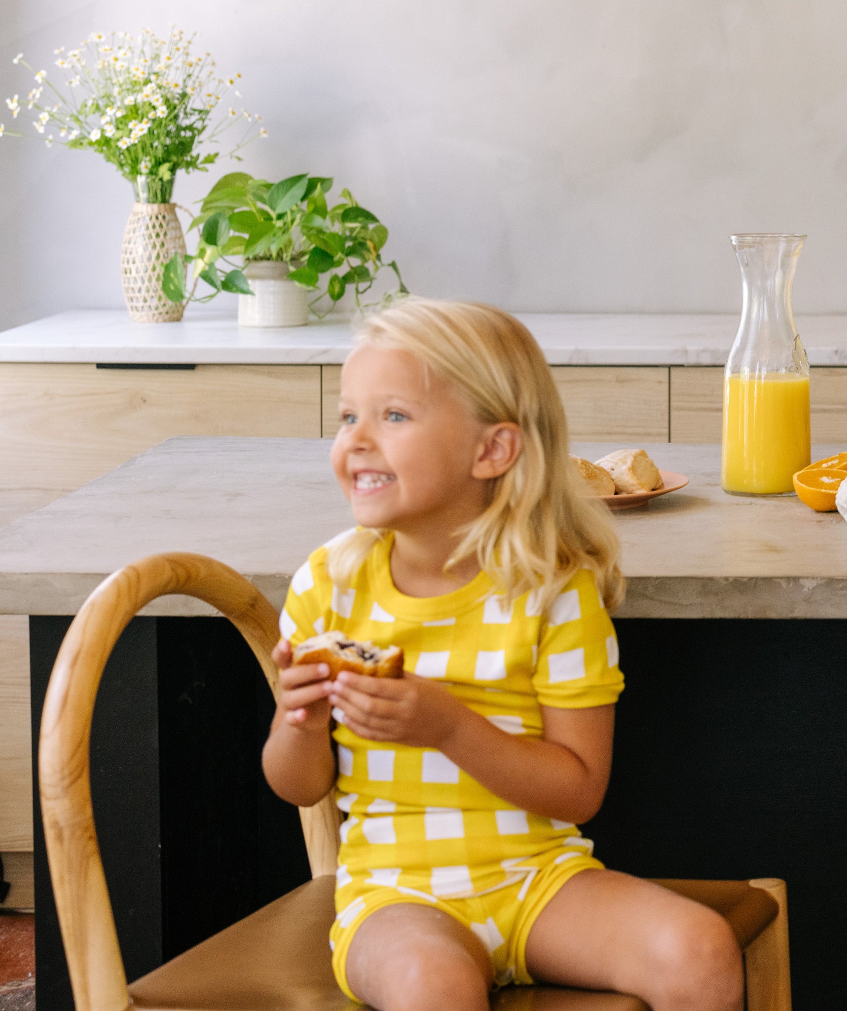 little girl wearing pajamas by la paloma in yellow gingham and eating a pastry for breakfast