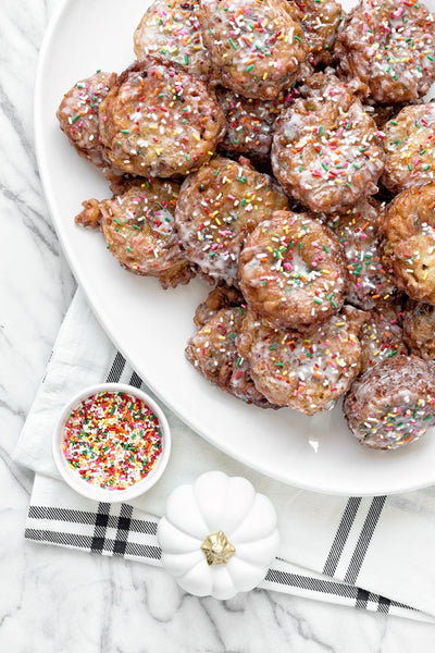 apple fritters on a serving platter with sprinkles and a small white pumpkin