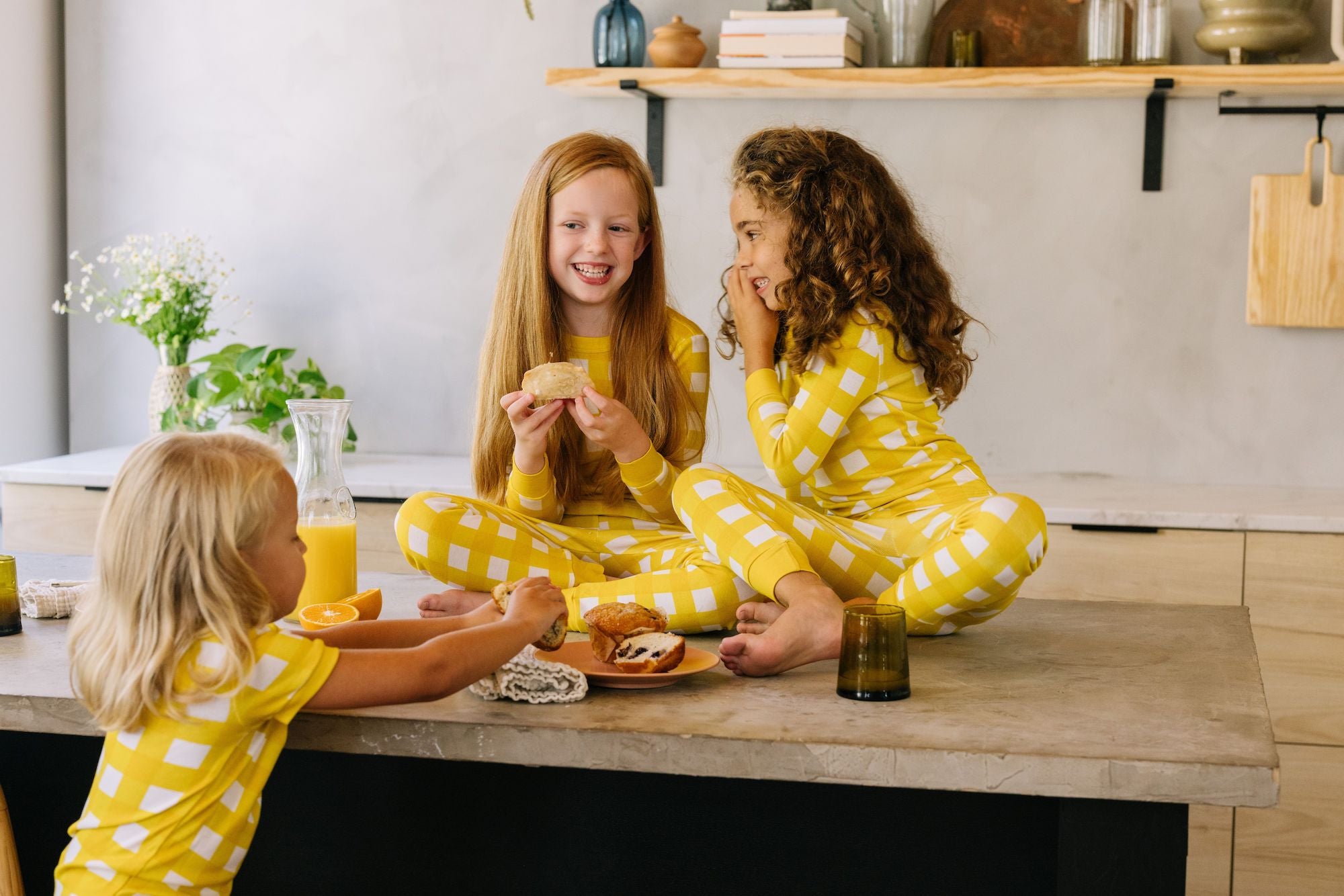 soft, yellow gingham pajama sets worn by two girls drinking orange juice and eating breakfast