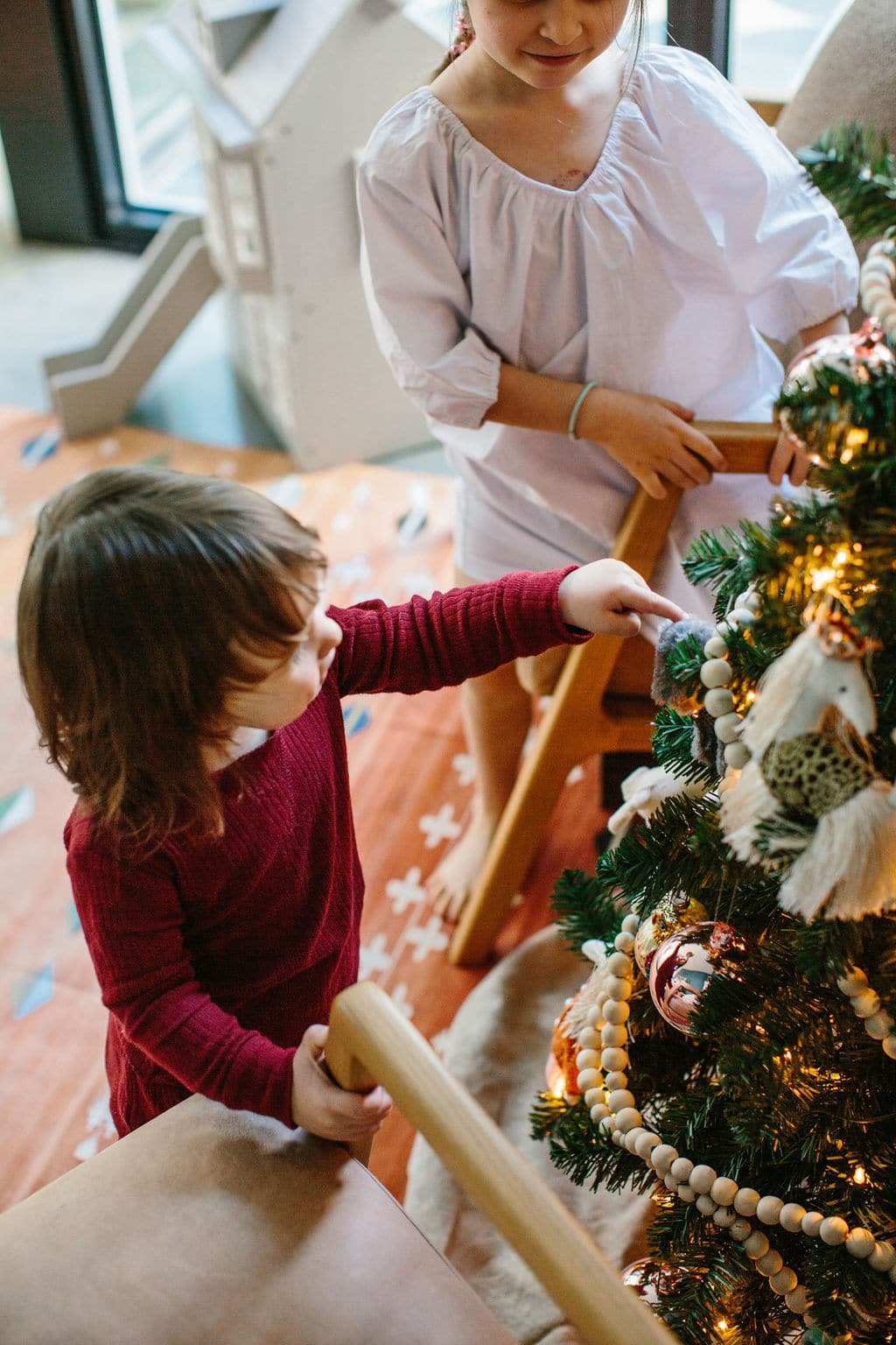 girl in cotton nightgown and sister in pajama set putting ornaments on christmas tree