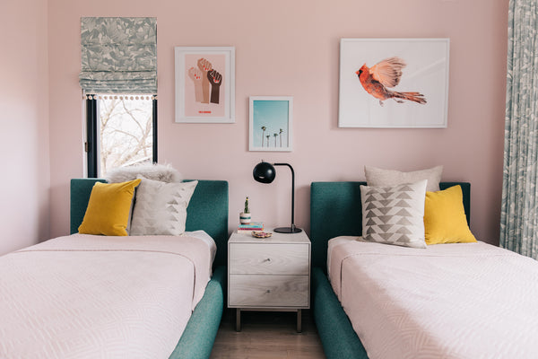 kids bedroom with two twin upholstered beds and pink quilts with a large bird photograph framed above one bed. 